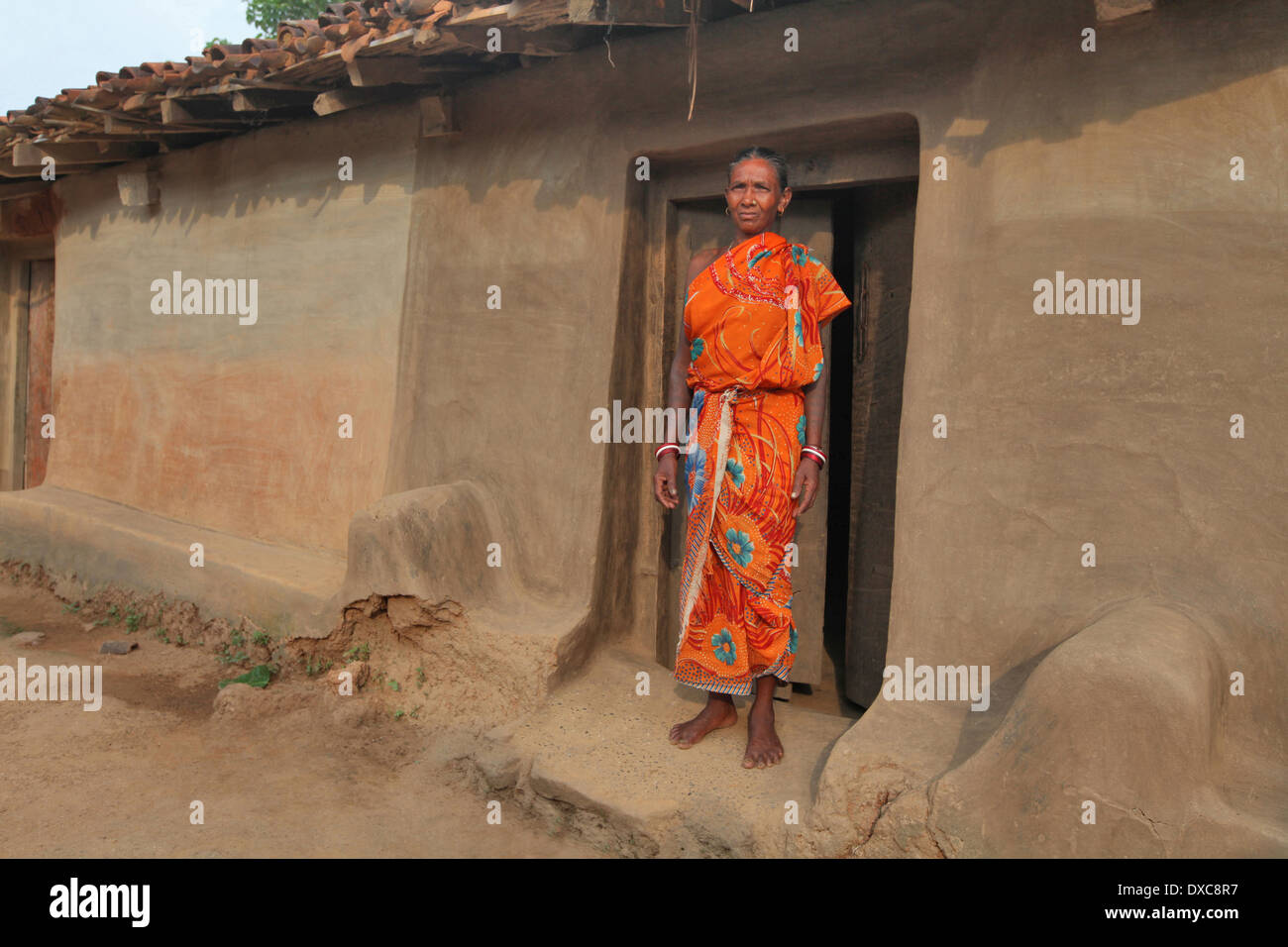 Femme en sari rouge debout devant sa maison de terre entrée. tribu santhal, Hardhekitand village, Jharkhand, India Banque D'Images