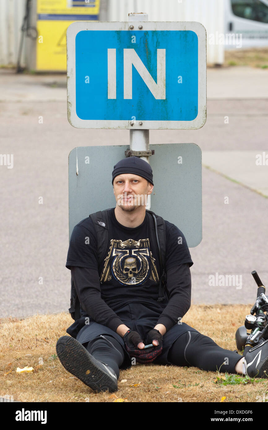Habillée tout en noir un cycliste fatigué se repose avec son dos contre un signe en Banque D'Images