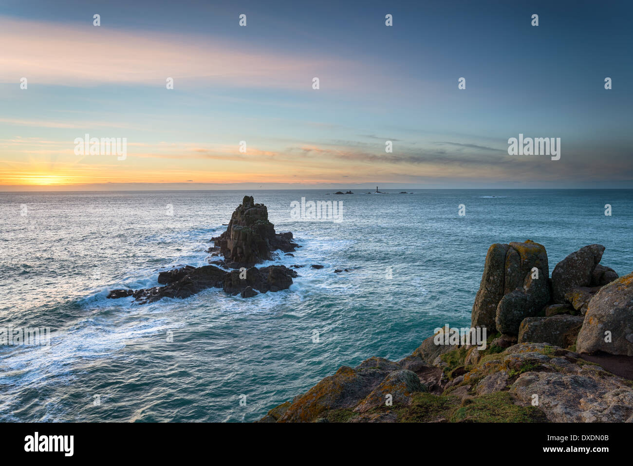 Des falaises rocheuses et des piles de la mer à Lands End en Cornouailles avec le phare au loin drakkars Banque D'Images