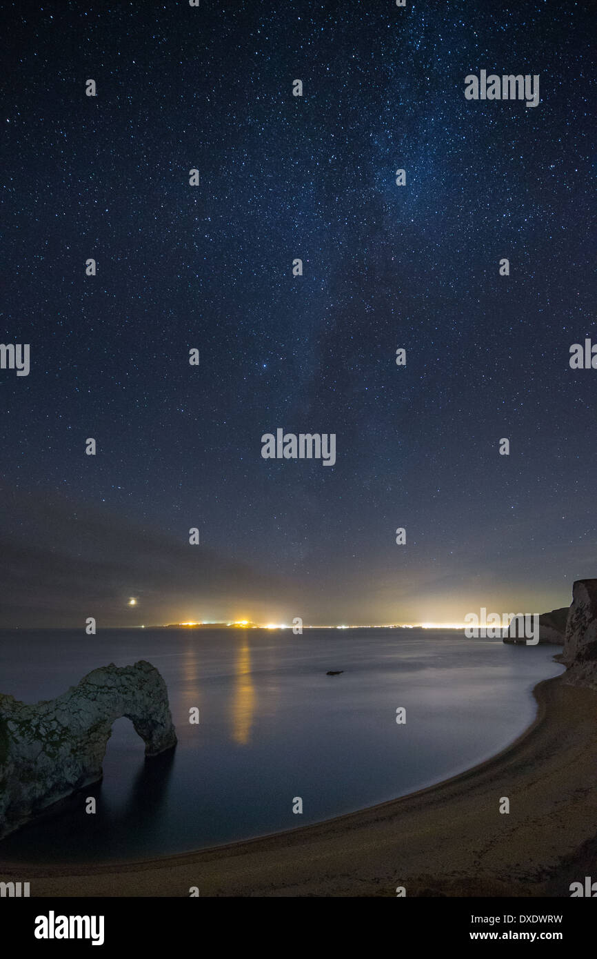 Les stars et Milky Way plus de Durdle Door et la Côte Jurassique, avec les lumières de Weymouth et Portland, Dorset, Angleterre au-delà Banque D'Images