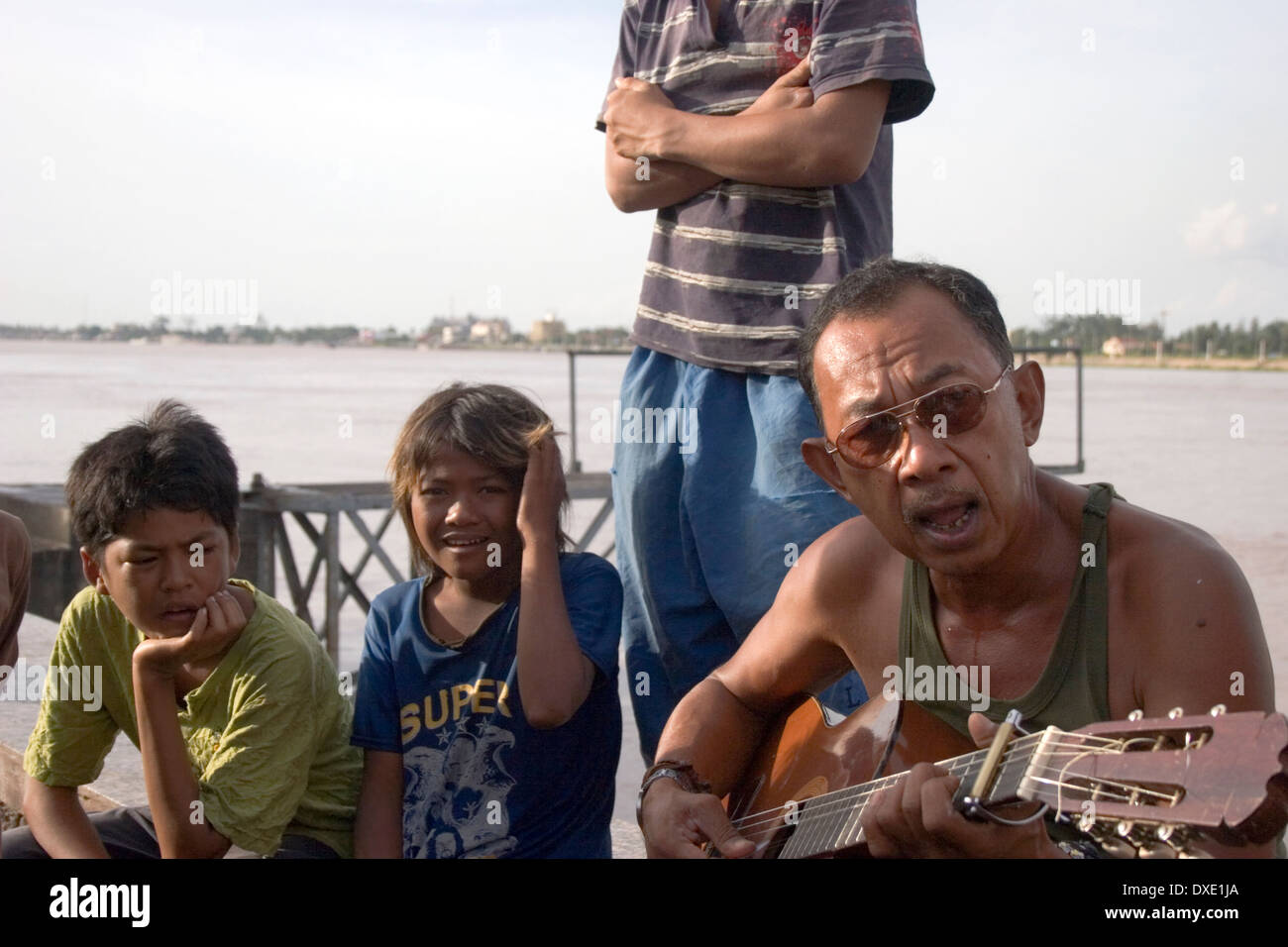 Un homme asiatique portant des lunettes de soleil est la lecture d'une guitare acoustique en bois sur les rives du Mékong à Phnom Penh, Cambodge. Banque D'Images