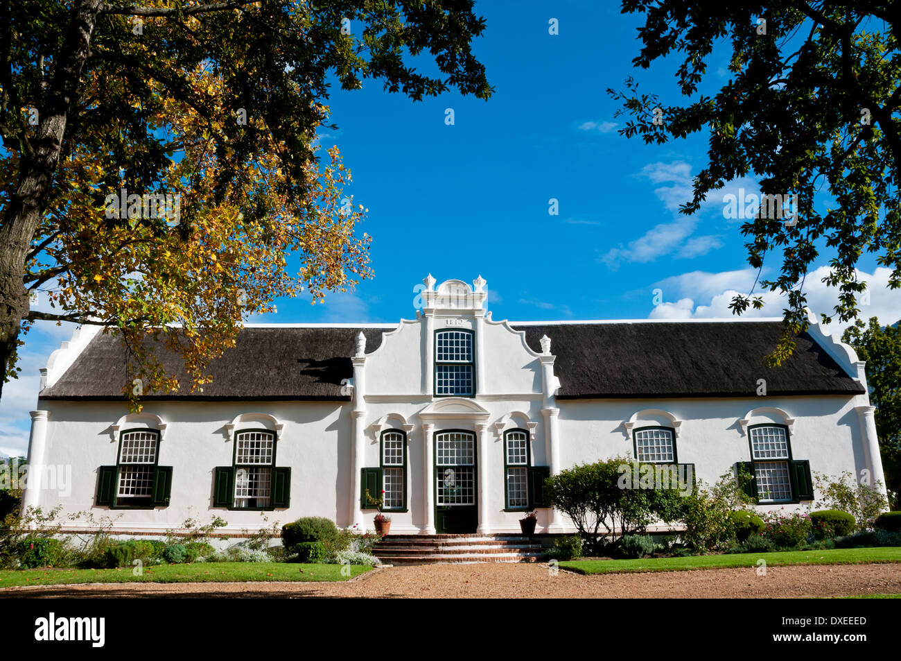 Manoir blanc sur une ferme viticole encadrées de feuilles automne couleur contre un ciel bleu dans le Western Cape, Afrique du Sud. Banque D'Images