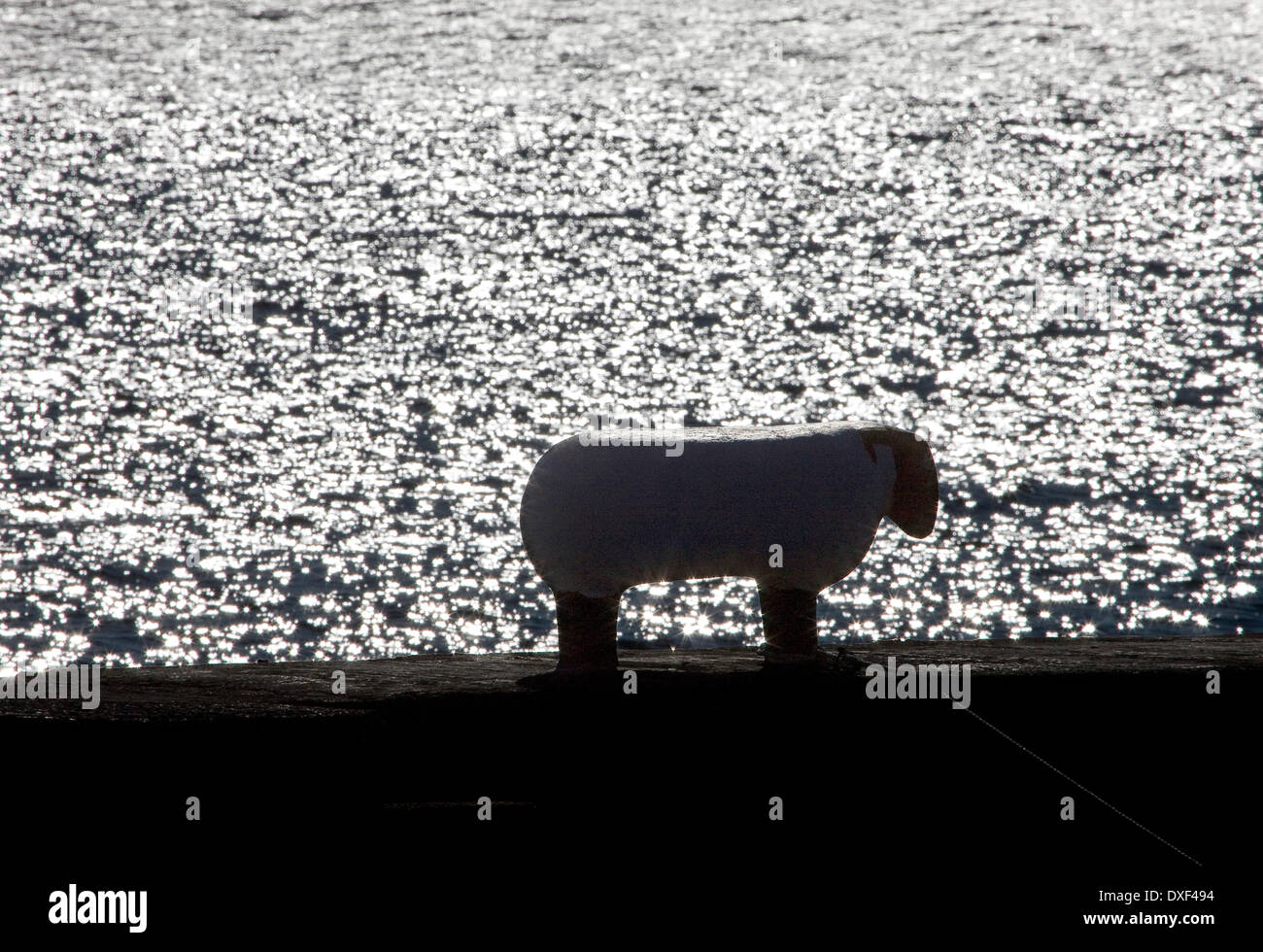 Une silhouette contre l'eau scintillante d'une brebis-Bollard sur la jetée en corrie village,Île d'Arran. Banque D'Images