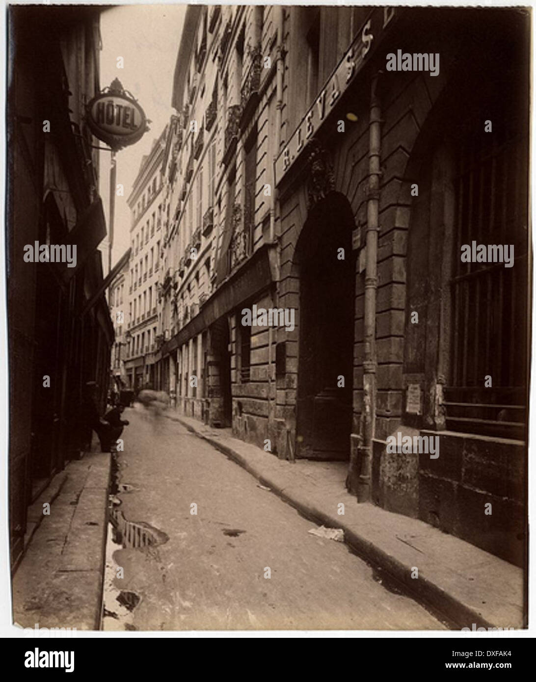 Photographie vintage de la rue Quincampoix à Paris, prise de la rue des Lombards. L’image offre un aperçu du paysage de rue et de l’architecture du 4ème arrondissement de Paris au cours des temps passés, mettant en valeur le tracé historique de la ville. Banque D'Images