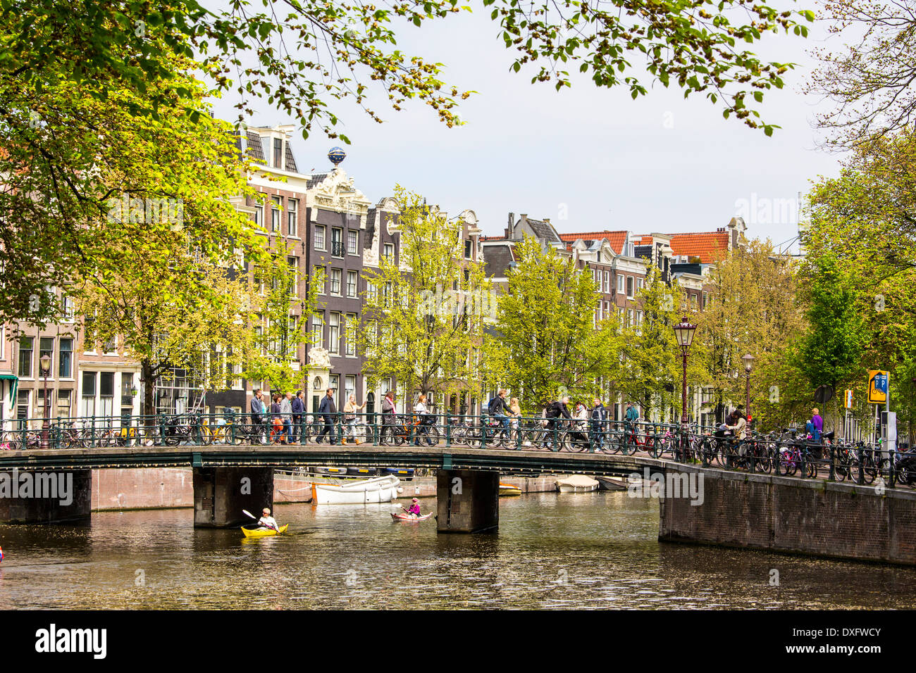 Les cyclistes et piétons traversant l'un des nombreux canaux d'Amsterdam comme deux canoës passer sous Banque D'Images