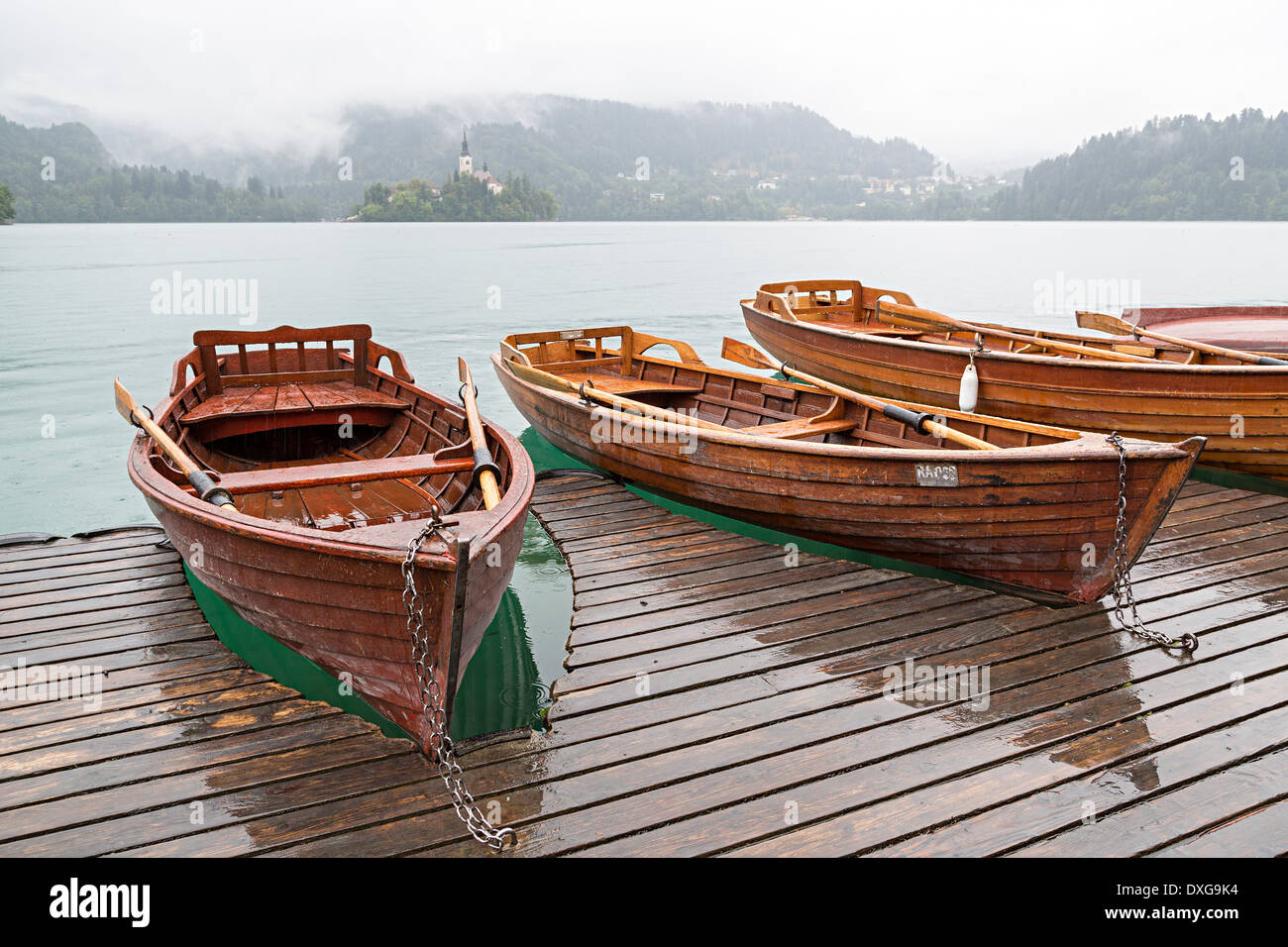 Barques sur la jetée sur le lac au Bled avec l'île et Mary église de pèlerinage dans la brume, Bled, Slovénie Banque D'Images