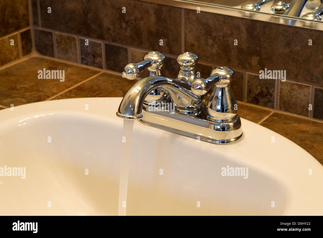 Photo horizontale de l'eau courante en robinet chrome salle de bains lavabo avec miroir partiel et tuile en arrière-plan Banque D'Images