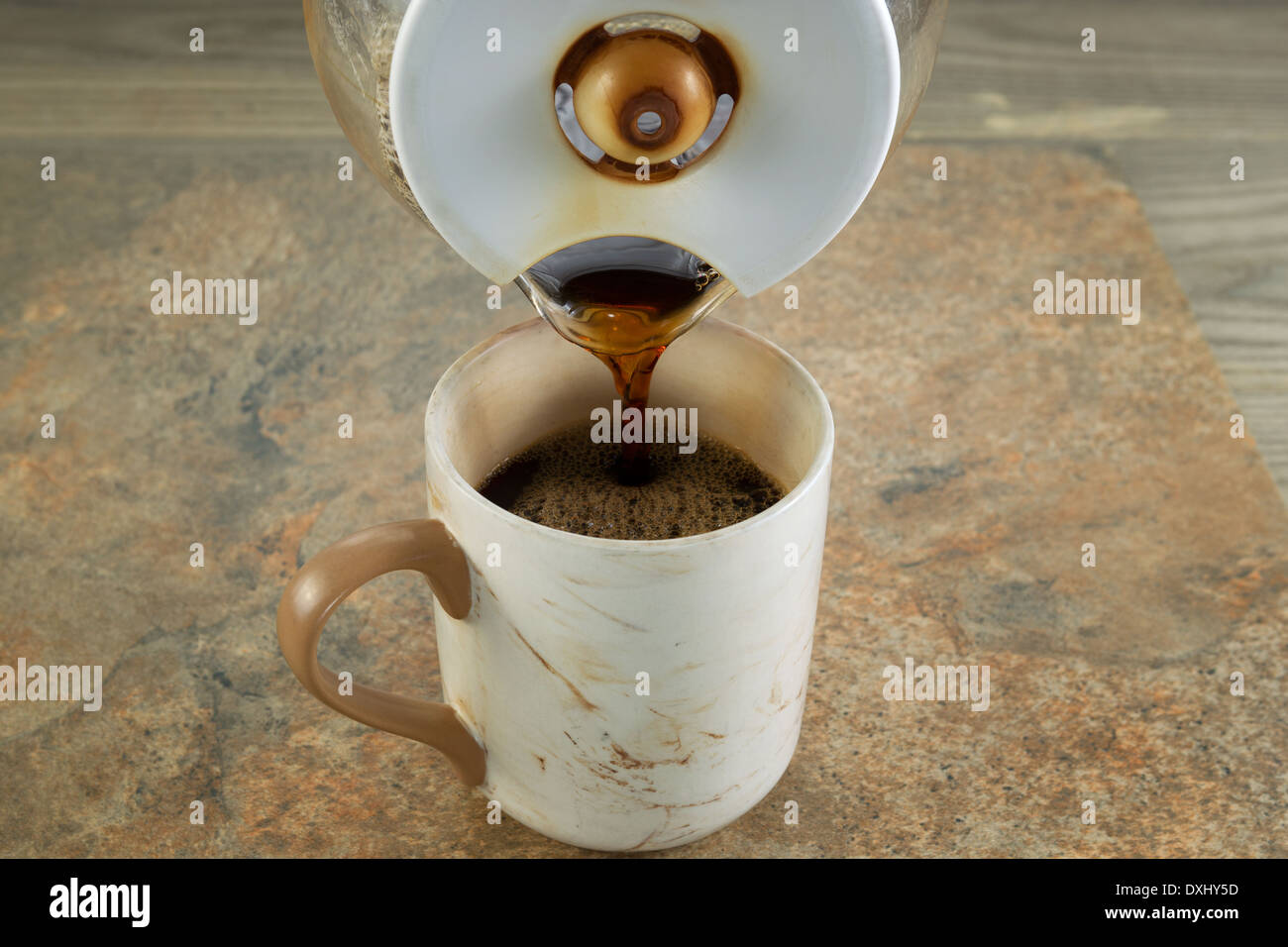 Photo horizontale de café noir fraîchement moulu est versé à partir de pot dans une tasse en céramique avec de la pierre et bois sous Banque D'Images