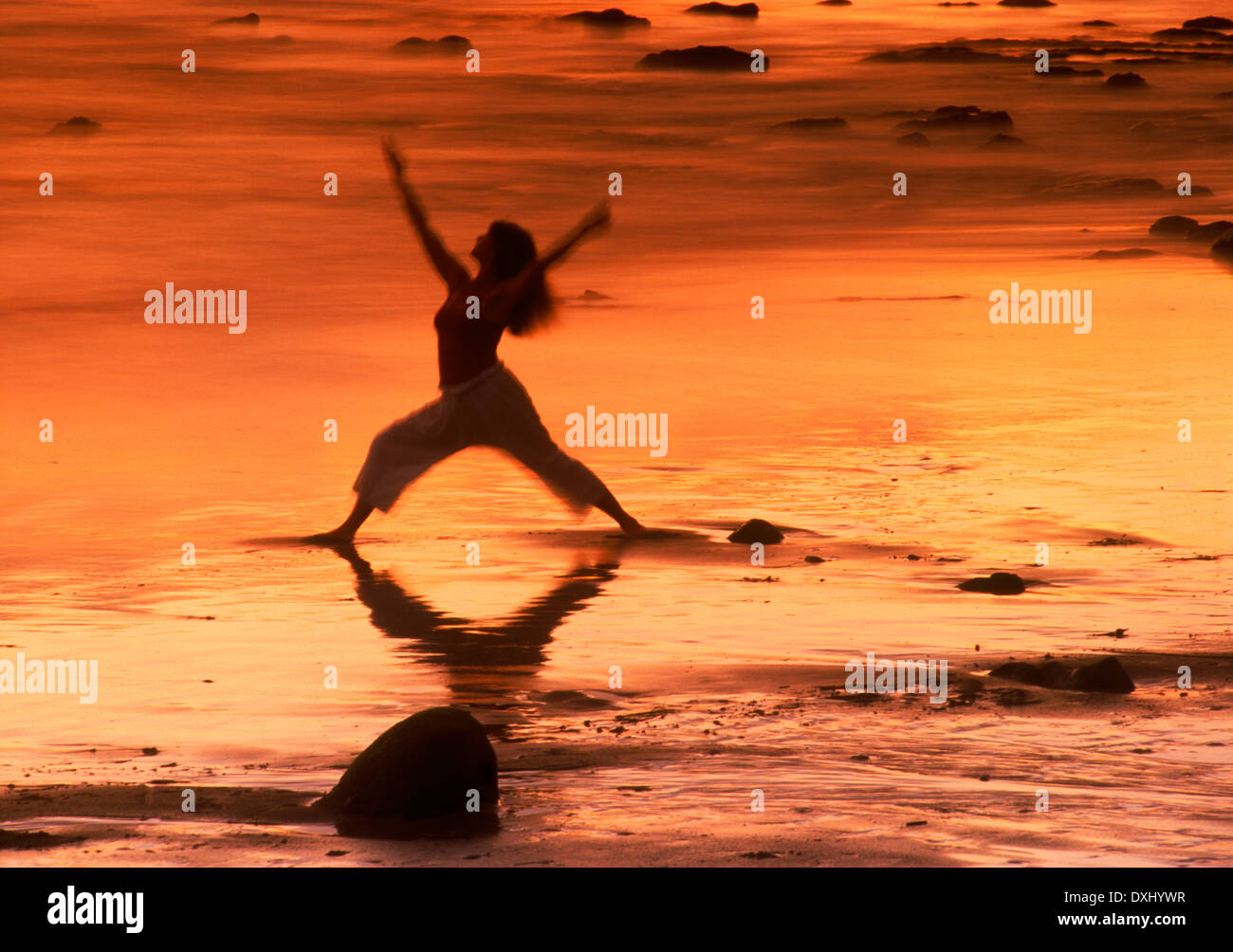 Woman in yoga position vague sur la rive peint au coucher du soleil Banque D'Images