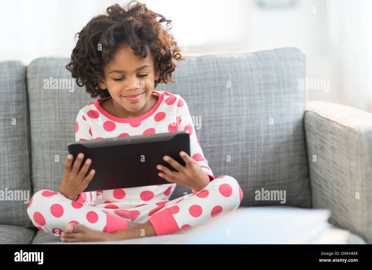 African American girl in pajamas using digital tablet on sofa Banque D'Images