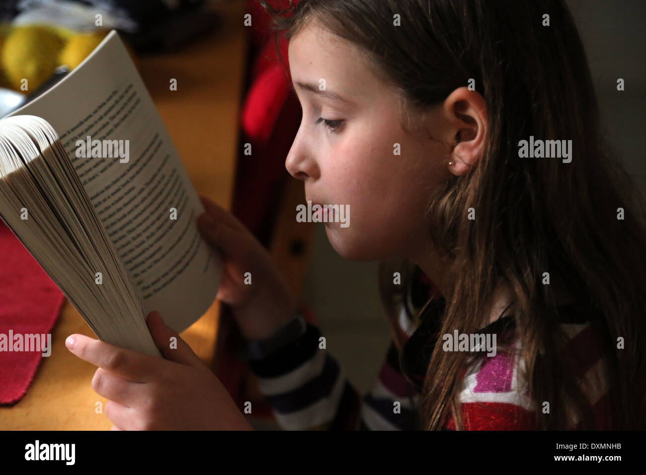 9 ans, fille, assis à table de cuisine La lecture d'un livre Ruby Redfort Surrey England Banque D'Images