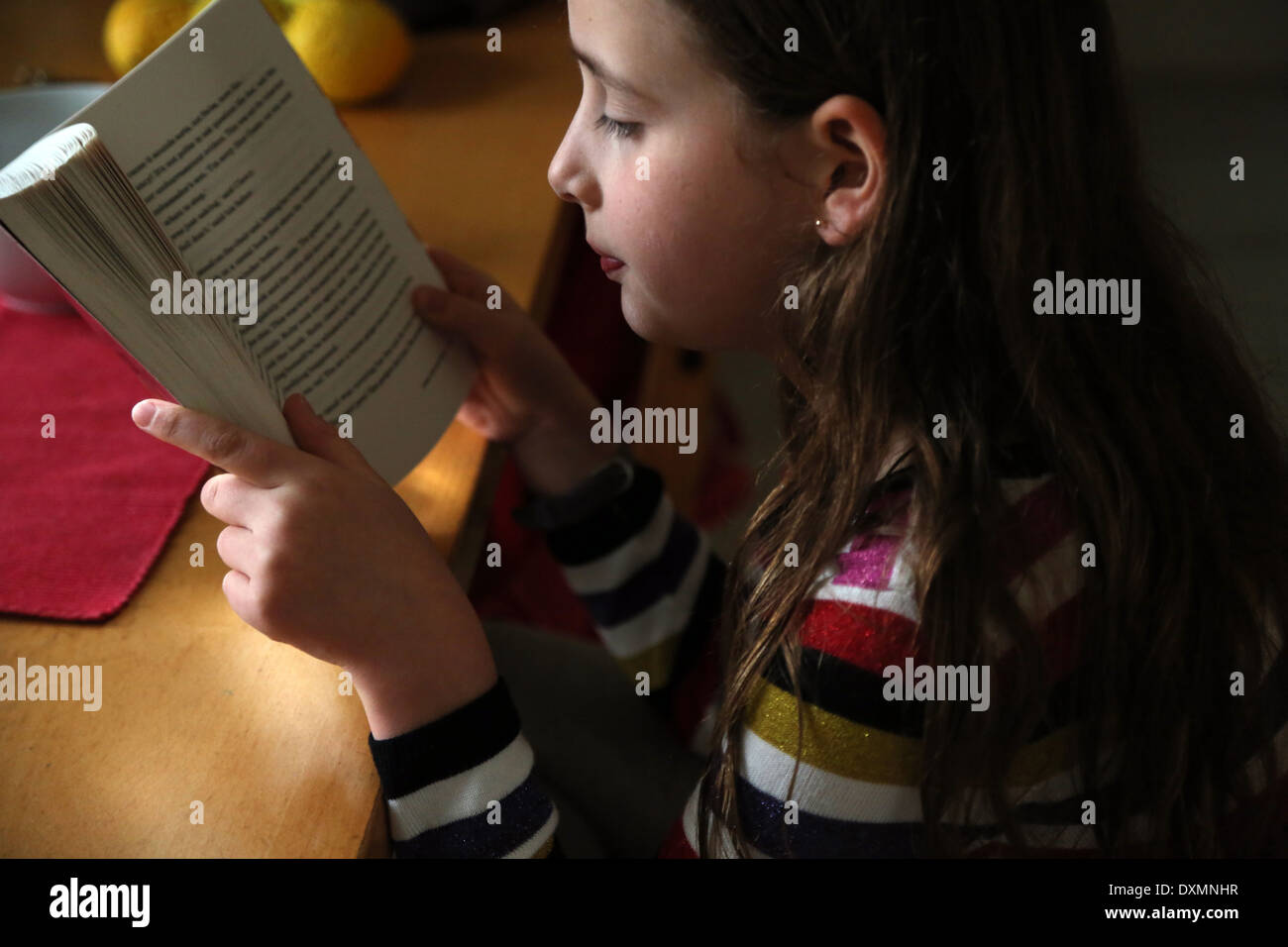 9 ans, fille, assis à table de cuisine La lecture d'un livre Ruby Redfort Surrey England Banque D'Images