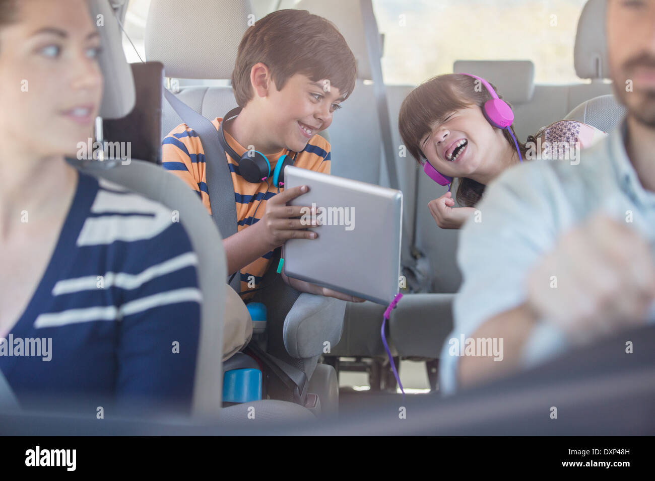 Happy brother and sister using digital tablet in back seat of car Banque D'Images