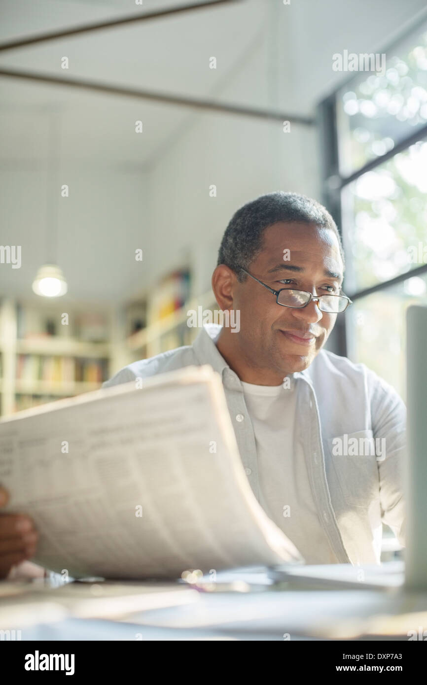 Senior man reading newspaper and using laptop Banque D'Images