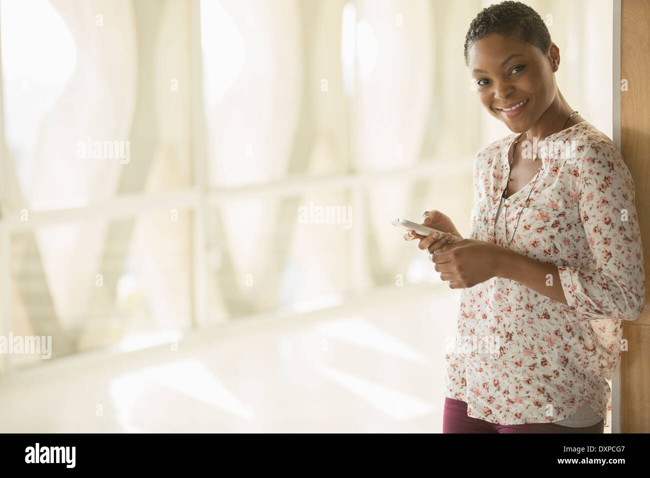 Portrait of smiling woman text messaging with cell phone in corridor ensoleillé Banque D'Images