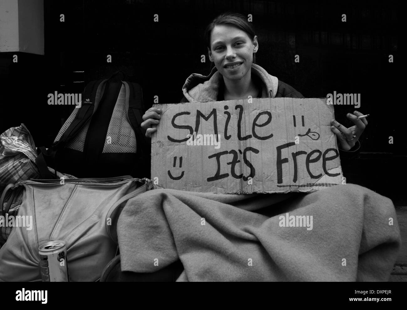 Homeless woman holding a sign & fumer une cigarette dans la rue à Londres. Banque D'Images