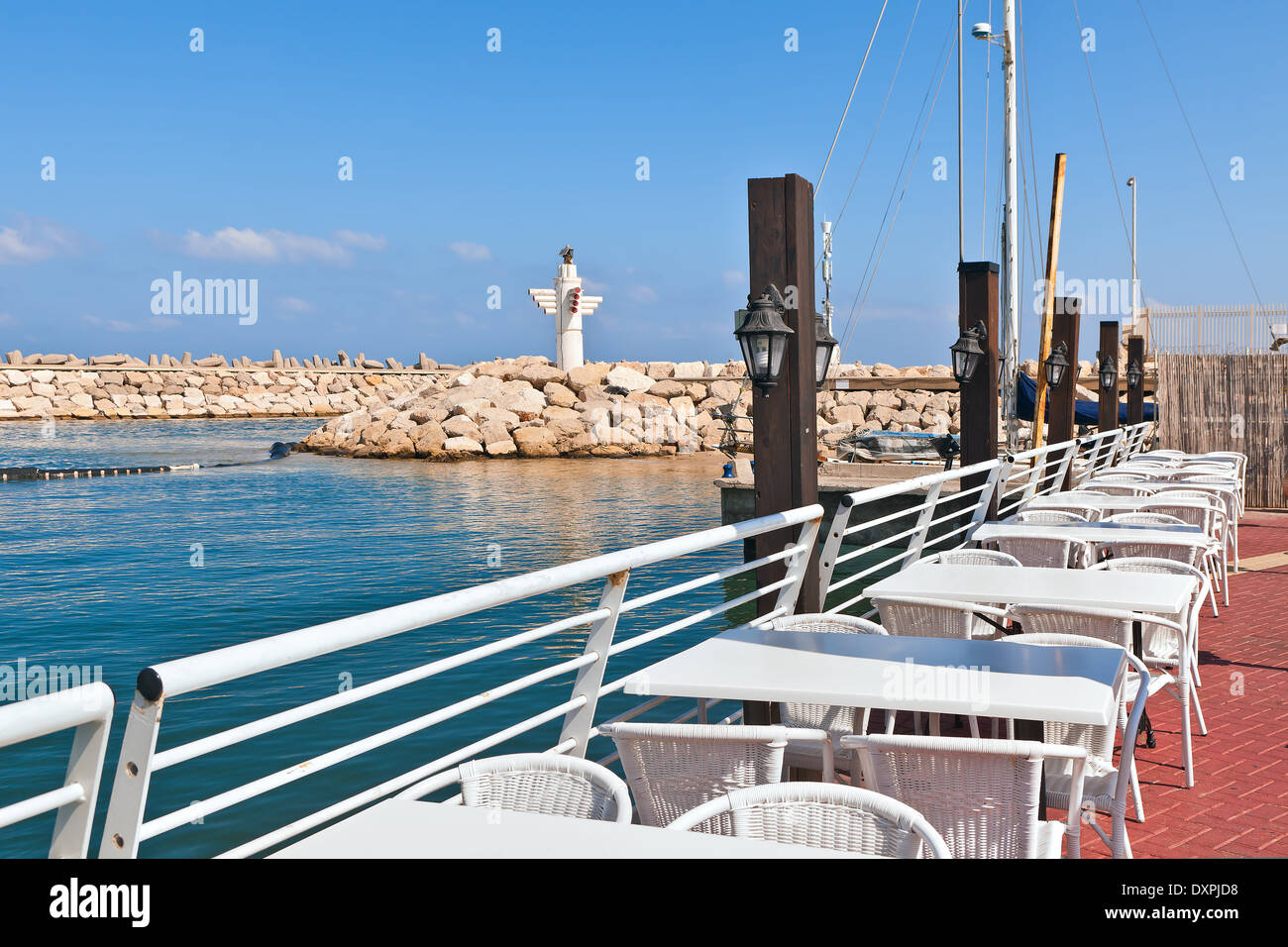 Restaurant en plein air sur les tables blanches le long de la promenade de marina et brise-lames avec phare à Ashkelon, en Israël. Banque D'Images