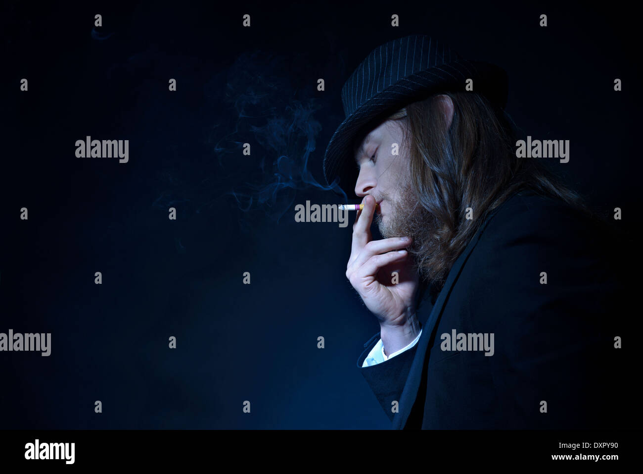 Cheveux longs barbus un homme portant un chapeau fedora et convenir à l'usage du tabac, un portrait de profil latéral avec traînée de fumée, un concept créatif Banque D'Images