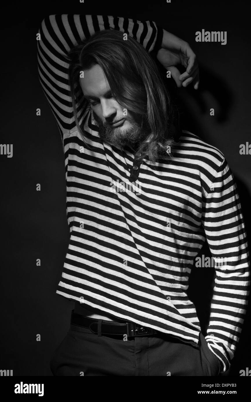 Un homme de perles, les cheveux longs, modèle masculin, posant dans un stripe shirt. Un noir et blanc sombre men's fashion portrait Banque D'Images