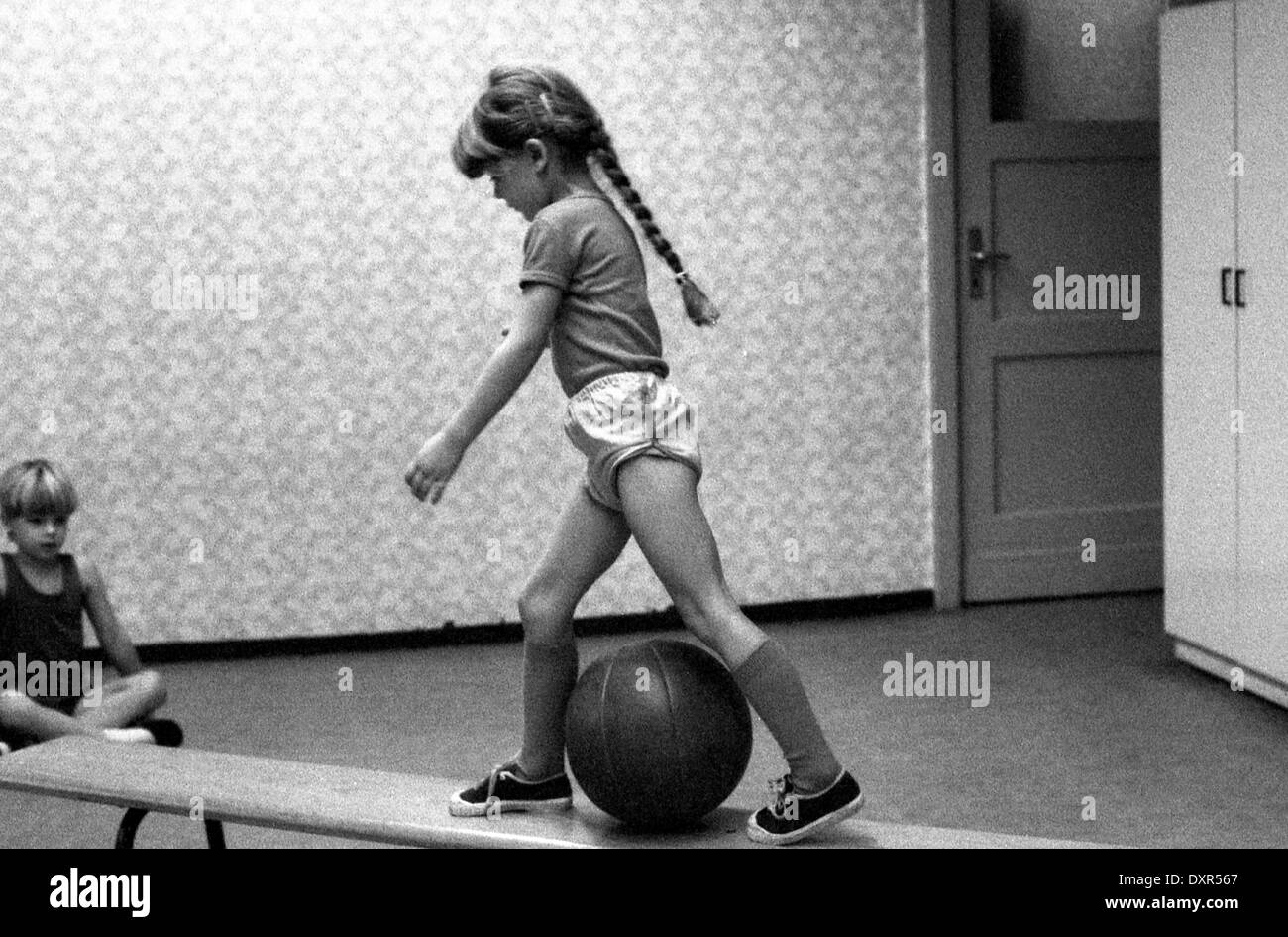 Berlin, DDR, petite fille augmente en éducation physique sur un banc sur un ballon Banque D'Images