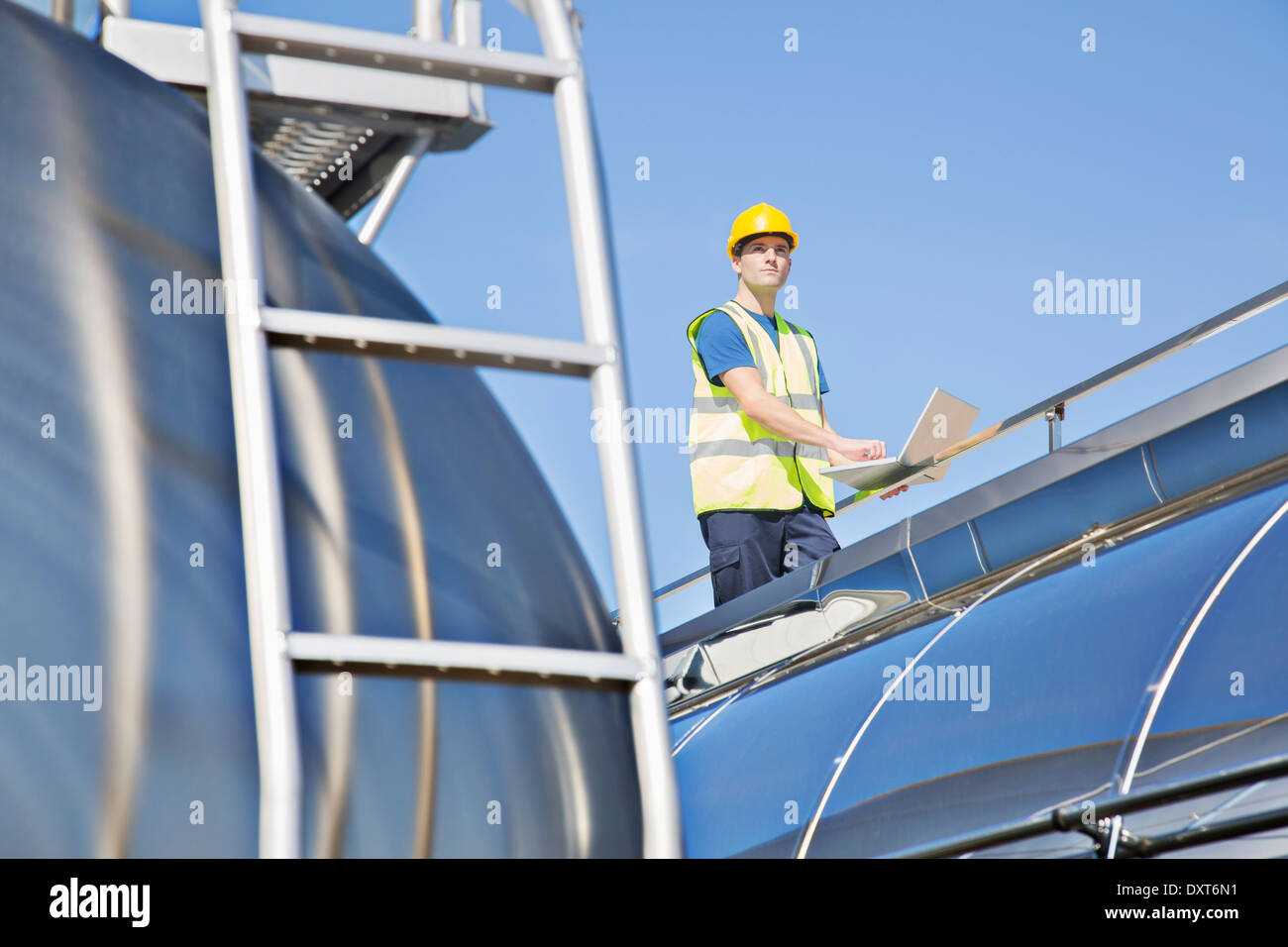 Worker using laptop sur la plate-forme au-dessus de citerne en acier inoxydable Banque D'Images