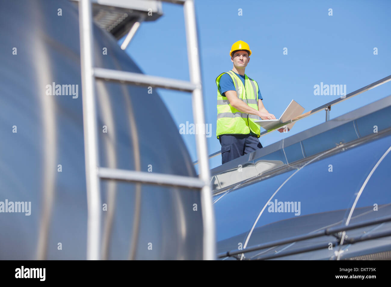 Worker using laptop sur la plate-forme au-dessus de citerne en acier inoxydable Banque D'Images