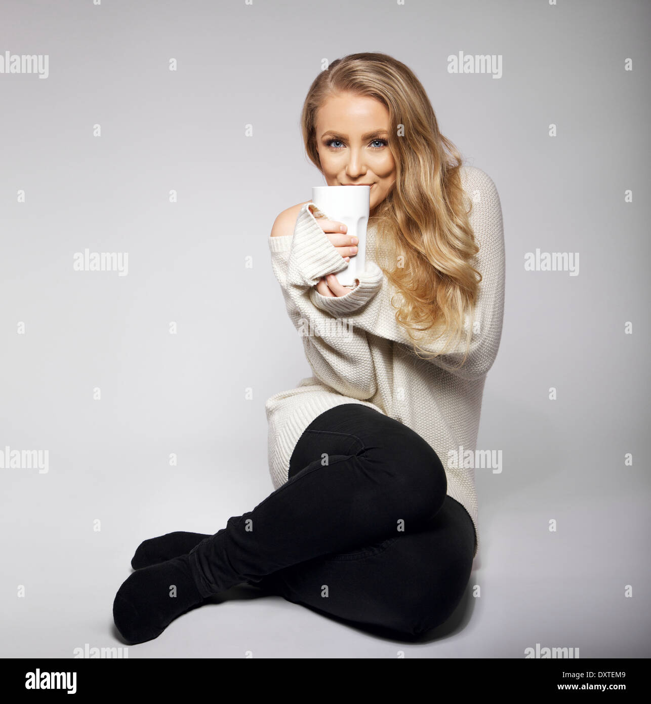 Mignon et belle jeune femme se réchauffer avec une bonne tasse de thé ou de café. Tourné sur fond gris. Blonde modèle. Banque D'Images