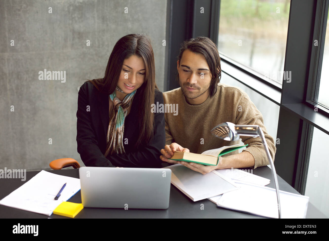 Jeune homme et femme avec ordinateur portable et livre se préparant aux examens. étudiants universitaires travaillant dur pour les examens finaux à la bibliothèque. Banque D'Images