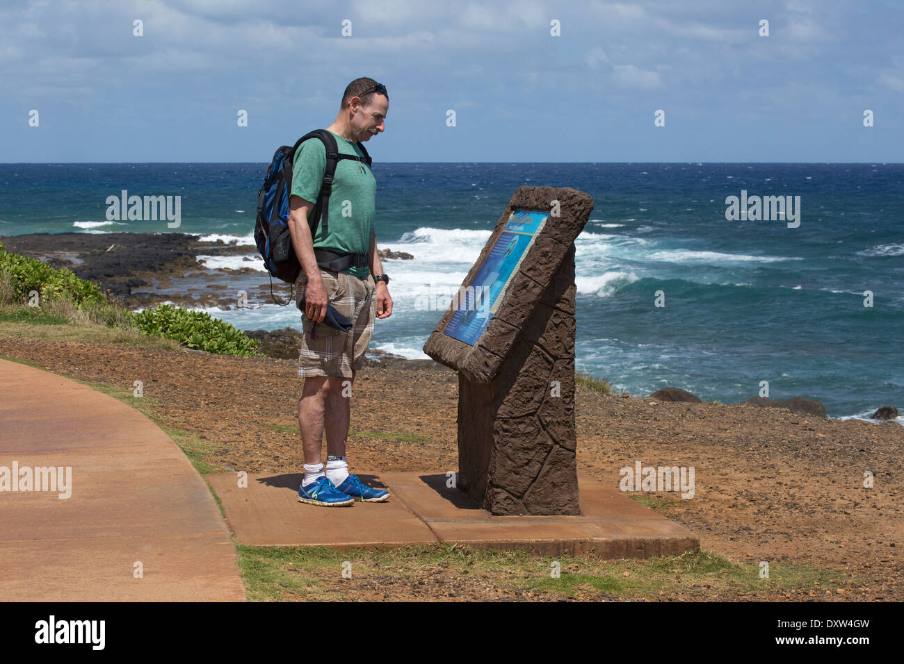 Faites de la place à un homme qui lit un panneau d'interprétation tout en marchant sur le chemin partagé de Kauai, Ke Ala Hele Makalae, le long de la côte océanique d'Hawaï. (60 ans) Banque D'Images
