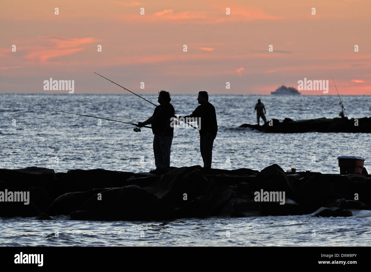 Les hommes la pêche au large de la plage au coucher du soleil à Cape May, NJ, USA Banque D'Images