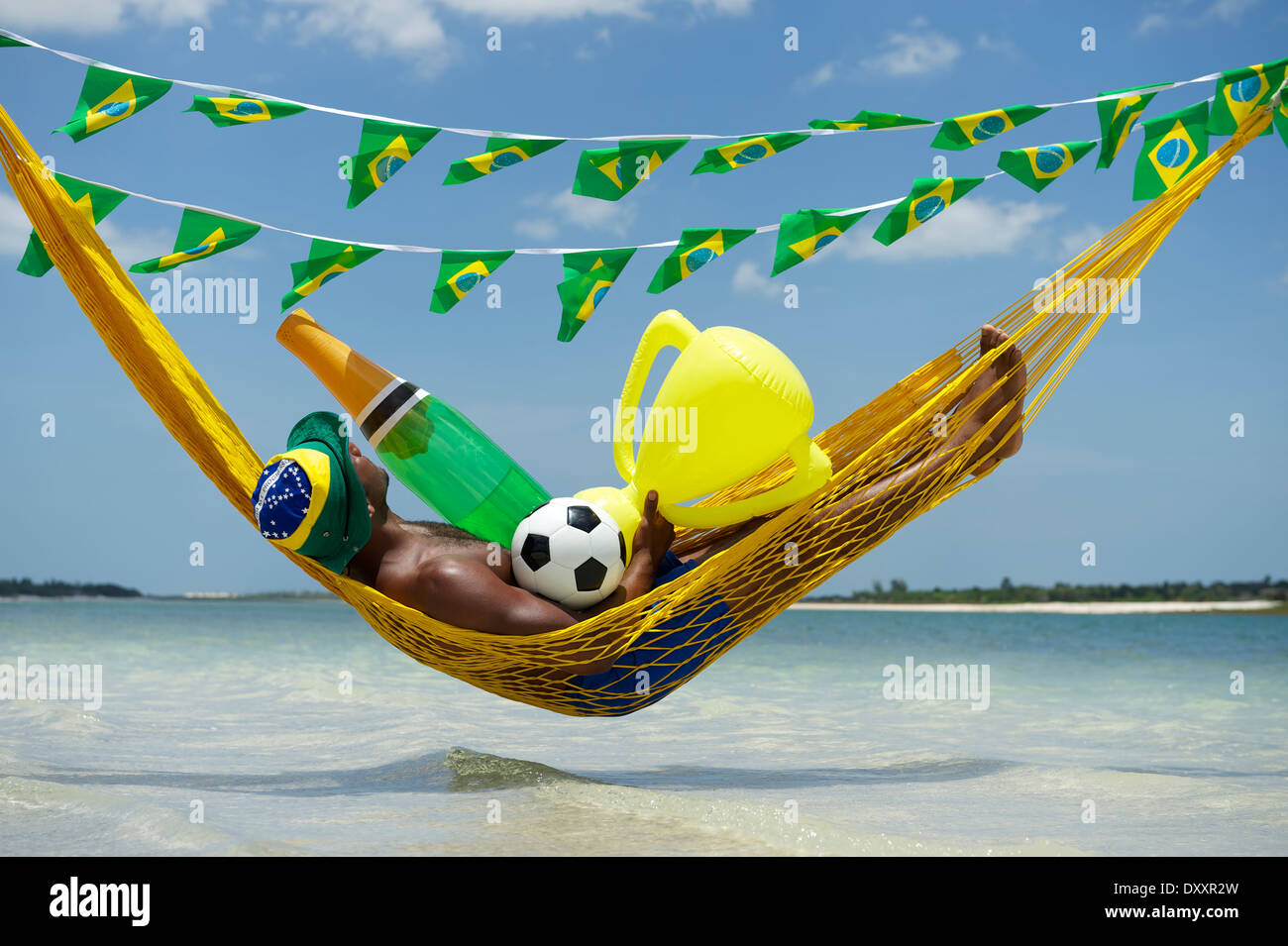 Brazilian soccer player célébrer en vous relaxant dans son hamac avec beach football, bouteille de champagne, et le trophée Banque D'Images