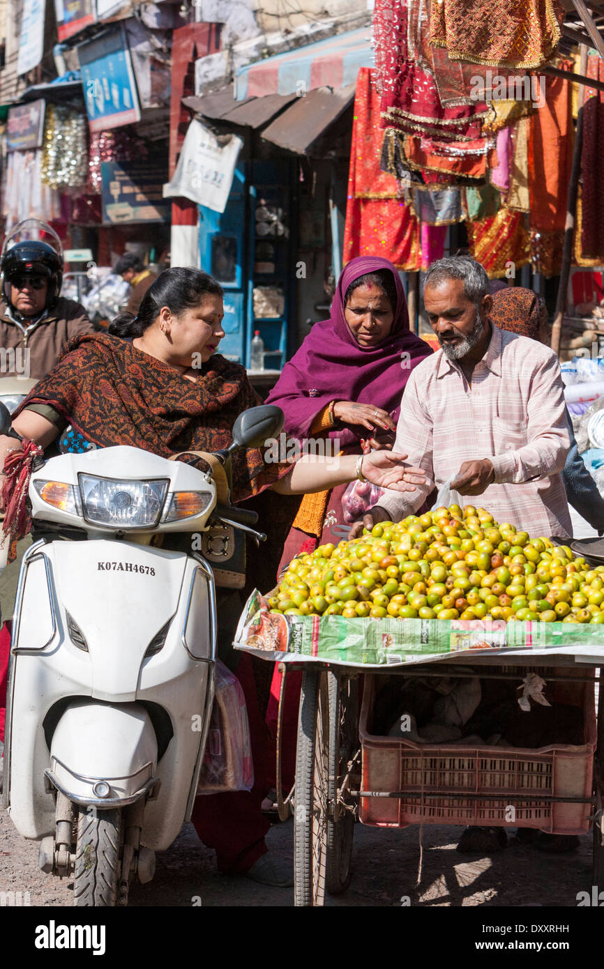 L'Inde, Dehradun. Femme sur moto acheter des fruits à un vendeur de rue. Banque D'Images