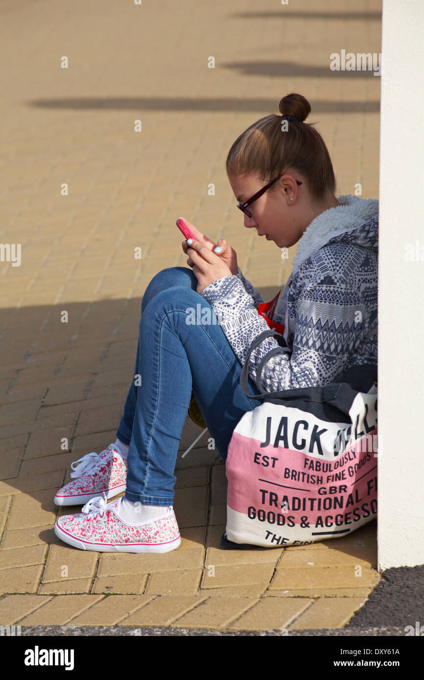 Fille assise sur le sol des sms sur le téléphone à Bournemouth en Mars Banque D'Images