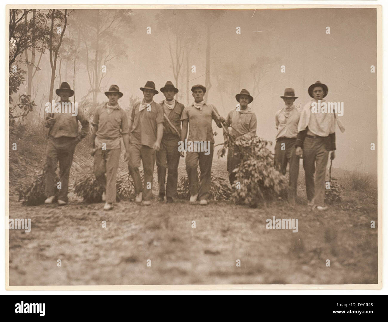 Cette photographie des années 1920, capturée par Sam Hood, montre des résidents et des volontaires combattant des feux de brousse en Australie, armés de branches vertes pour aider à contenir les flammes. Il met en lumière les efforts de la communauté pendant la saison dévastatrice des feux de brousse. Banque D'Images