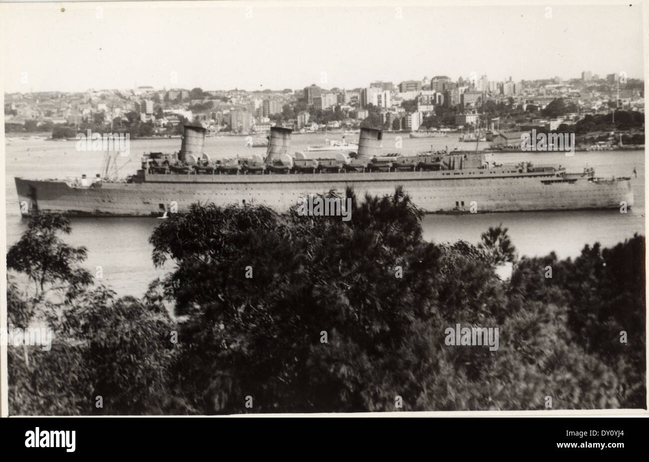 Le RMS Queen Mary, un navire de troupes britannique, est photographié à Sydney pendant la IIe Guerre mondiale. L'image met en évidence le rôle du navire dans le transport de troupes et de fournitures pendant la guerre, avec l'emblématique marque Cunard Line visible. Le Queen Mary reste l'un des paquebots les plus célèbres de l'histoire. Banque D'Images