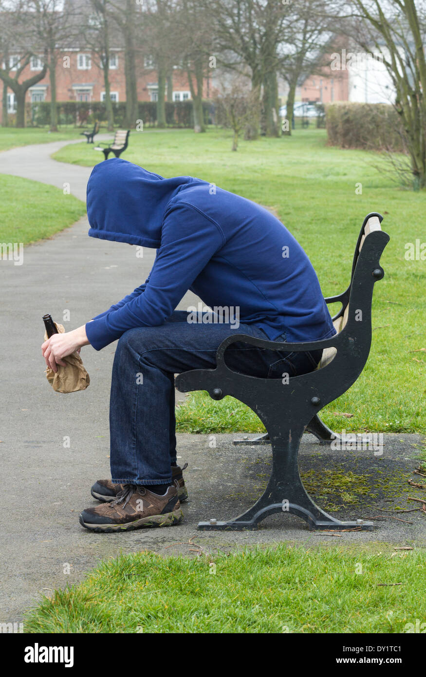 Homme portant des sweat assis sur banc de parc de boire de l'alcool Banque D'Images