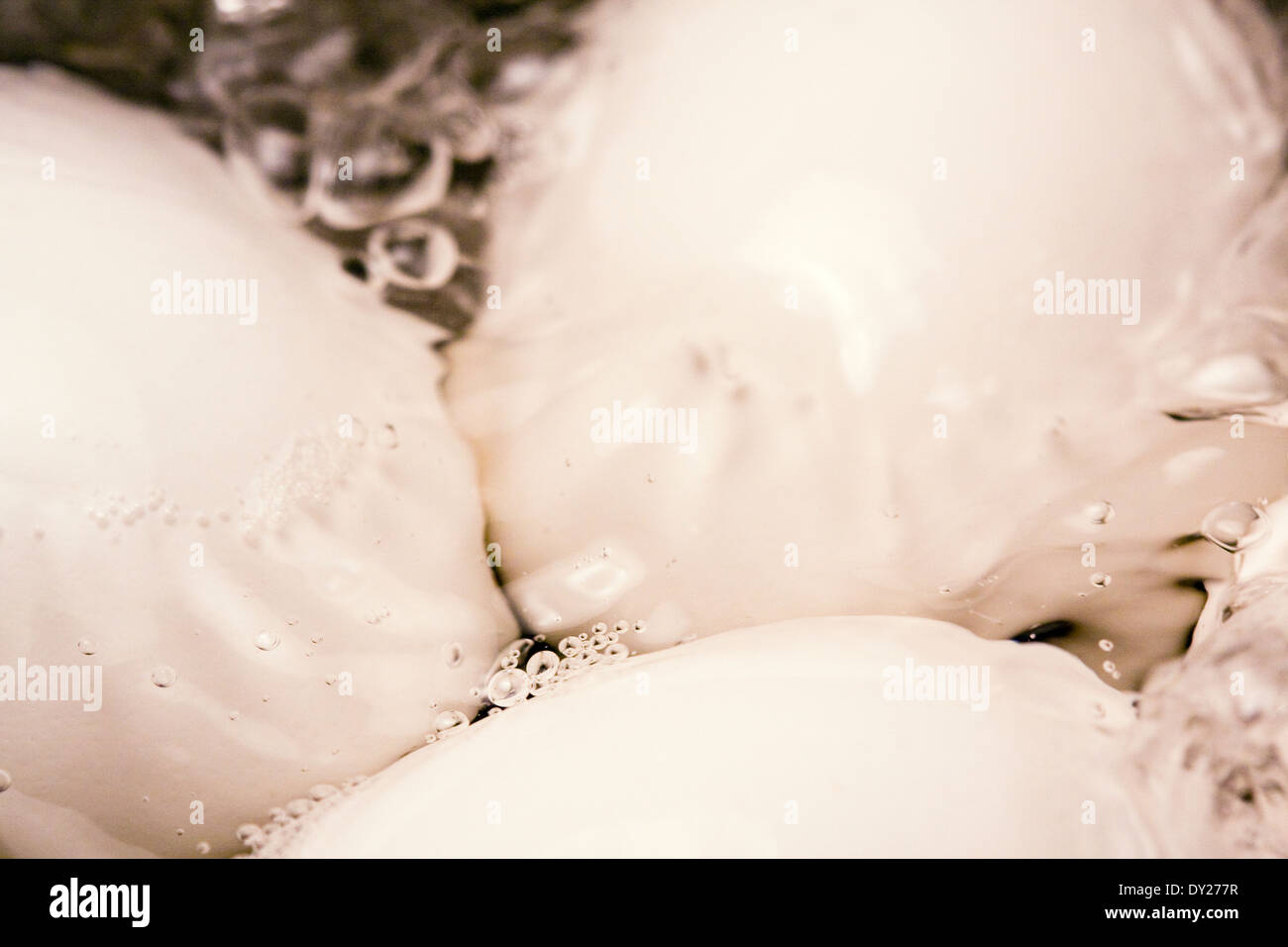 Des bulles apparaissent à la surface de l'eau bouillante comme trois œufs blancs sont cuits dans un pot Banque D'Images