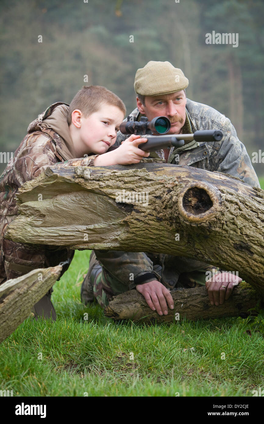 Un jeune garçon avec une carabine dans la campagne avec son père garde-chasse à côté de lui. Banque D'Images