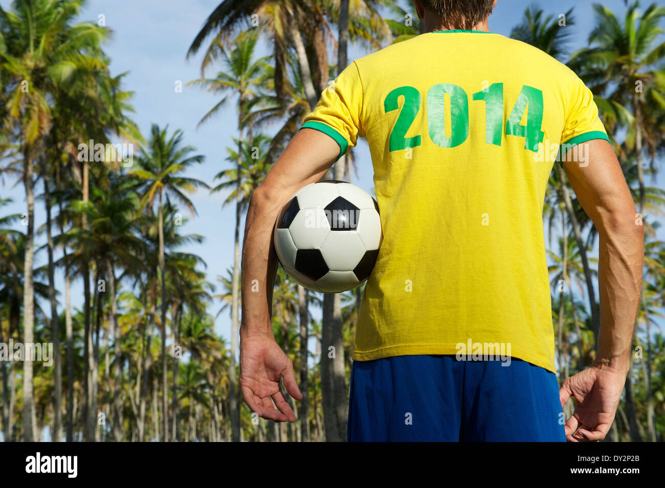 Joueur de football brésilien au Brésil en permanent uniforme couleurs bosquet de palmiers tropicaux holding soccer ball Banque D'Images