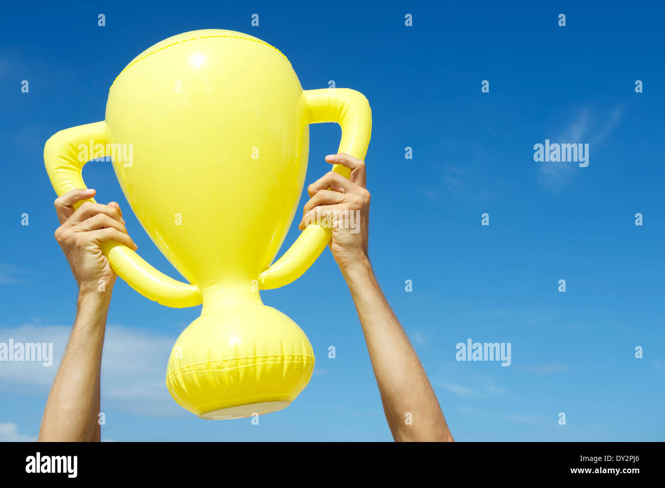 Mains de champion gagnant holding trophy jaune gonflable dans ciel bleu Banque D'Images