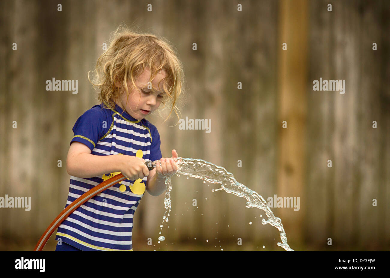 Garçon jouant avec le tuyau d'eau dans le jardin Banque D'Images