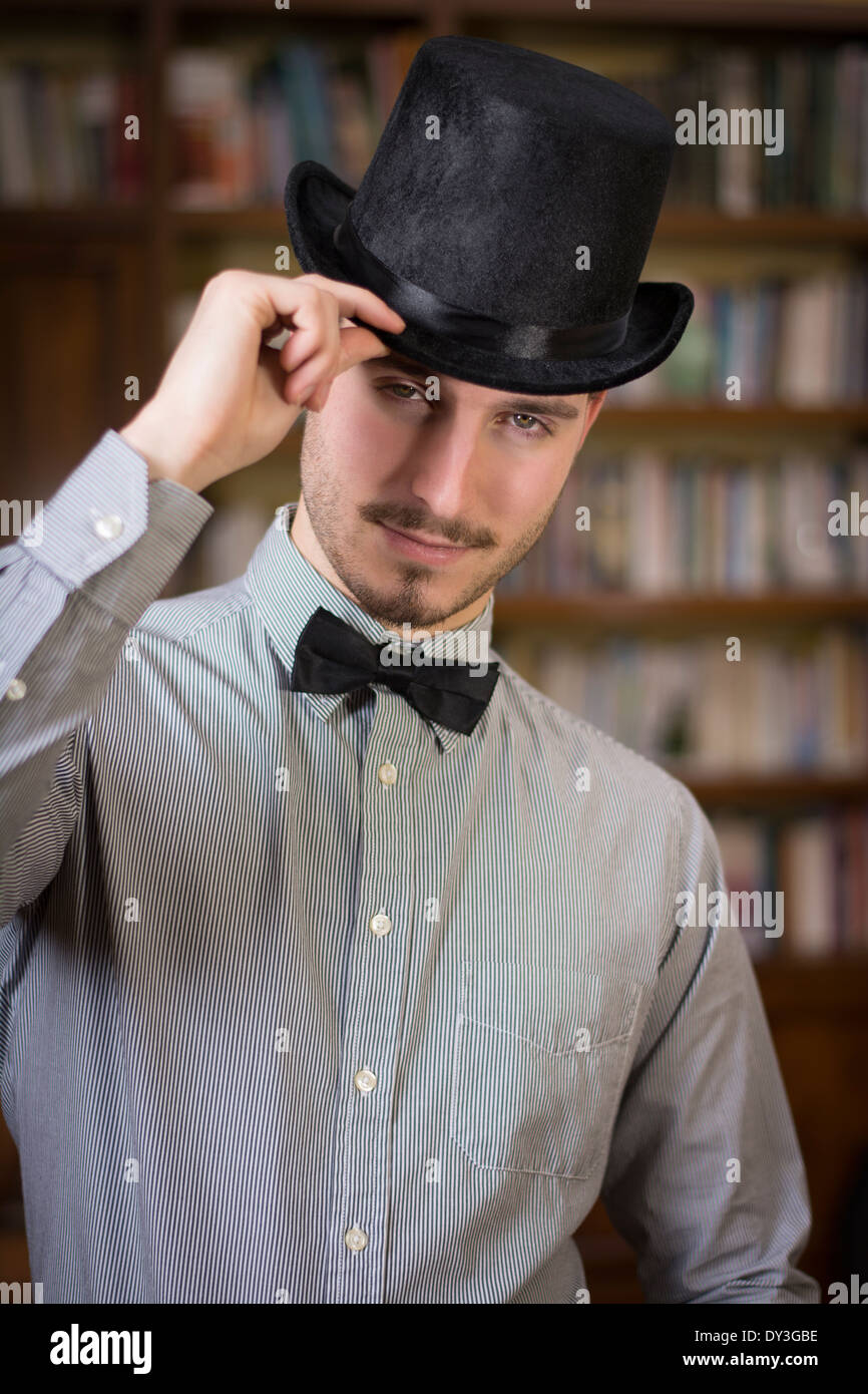 Séduisant jeune homme portant un chapeau haut de forme et noeud papillon,  looking at camera. Tourné à l'intérieur Photo Stock - Alamy