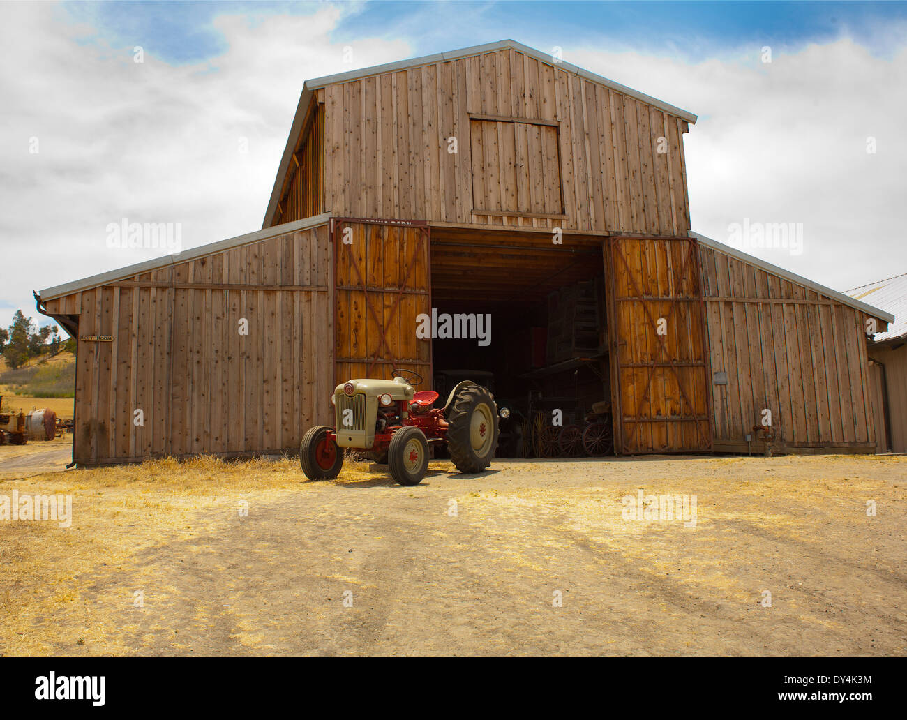 Une ancienne grange non peinte en bois, portes ouvertes et le tracteur garé devant. Banque D'Images