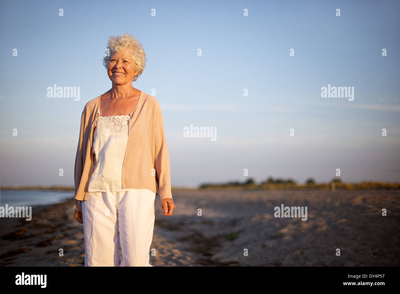 Portrait of happy young woman standing at the beach looking at camera. Vieille dame souriant tout seul sur la plage. Banque D'Images