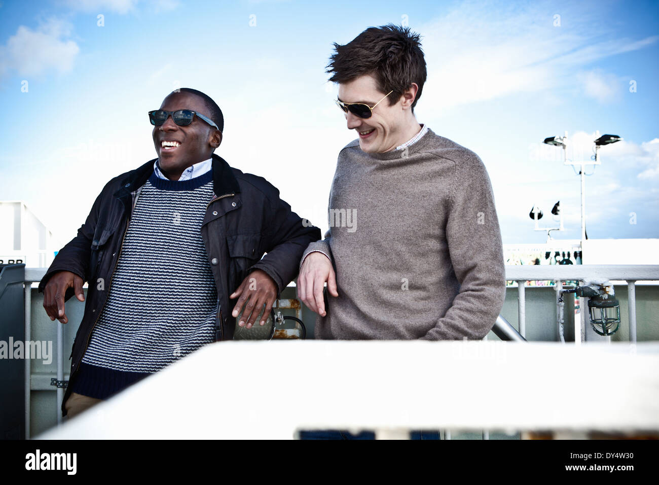 Les amis masculins leaning against fence chatting Banque D'Images