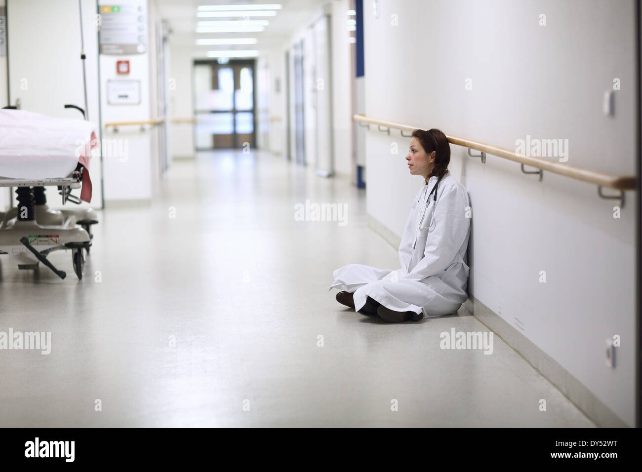 Female doctor sitting cross legged in hospital corridor Banque D'Images