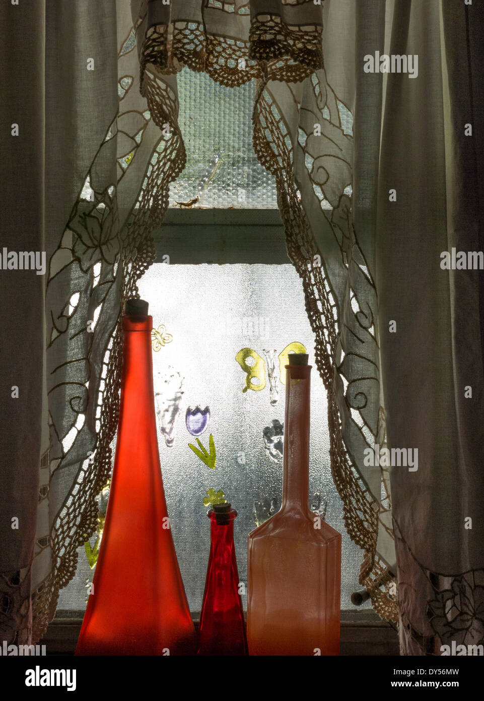 Verser la lumière du soleil dans une fenêtre d'accueil de la banlieue et des rideaux décoratifs en verre rouge sur des flacons de parfum anciens, USA Banque D'Images