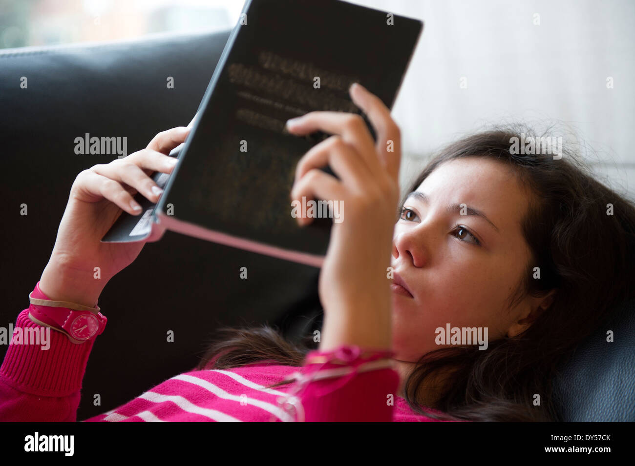 Girl lying on sofa, reading book Banque D'Images