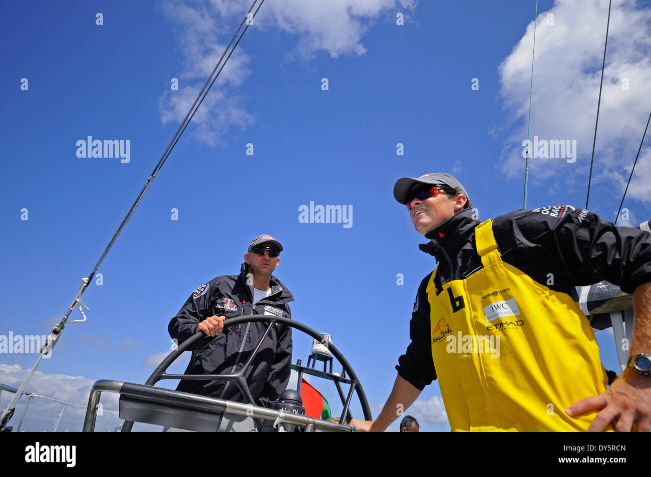 Skipper à la roue d'un bateau de course avec un équipage homme debout à proximité, les deux portant des lunettes de soleil et casquettes under blue sky Banque D'Images