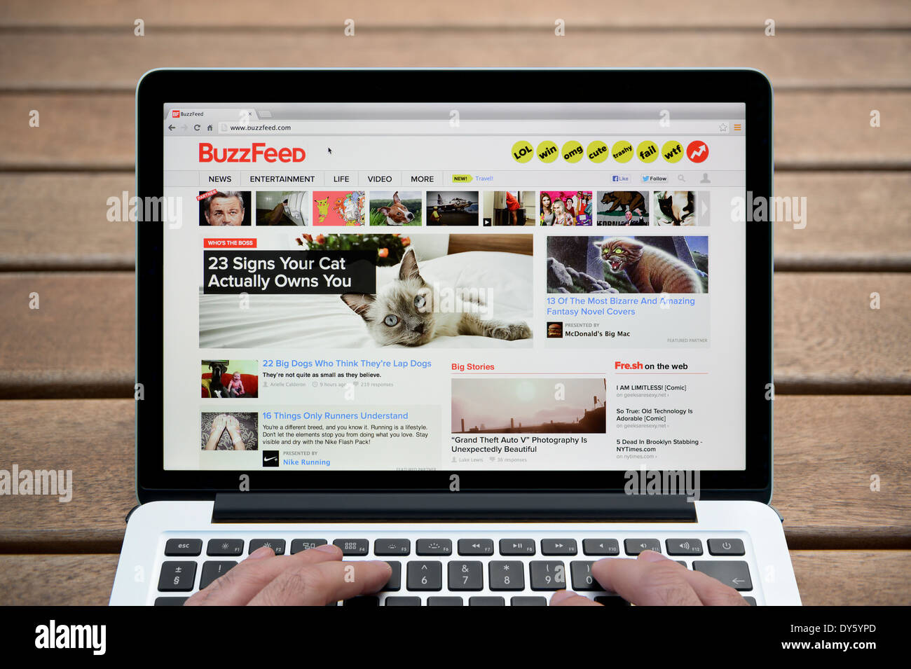 Le site BuzzFeed sur MacBook contre un banc en bois fond de plein air y compris les doigts d'un homme (usage éditorial uniquement). Banque D'Images